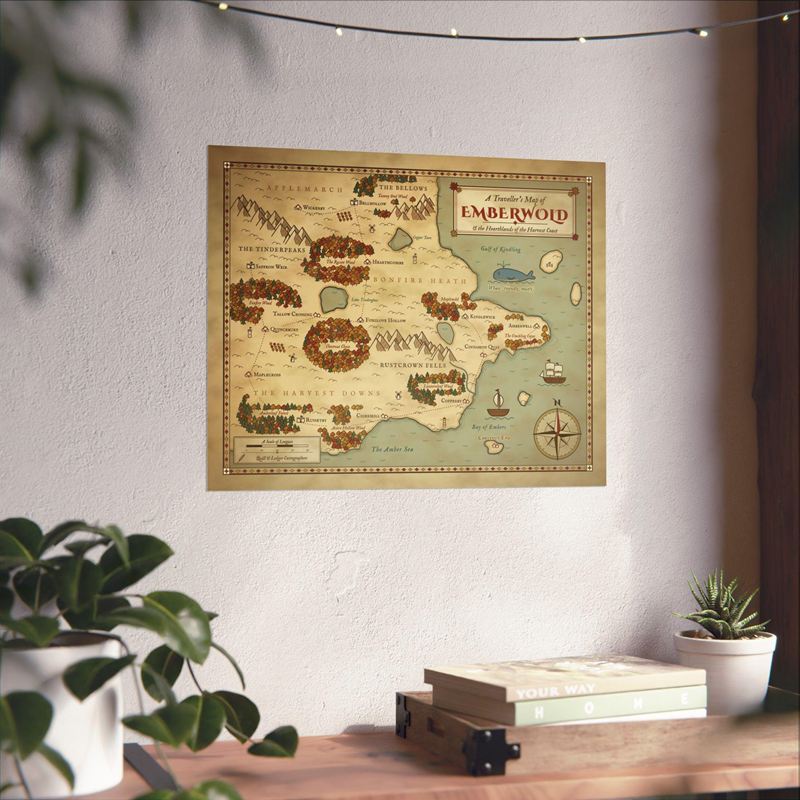 Autumn fantasy map print of a coast with russet woods, mountains and a whale, on a wall above a desk with plants
