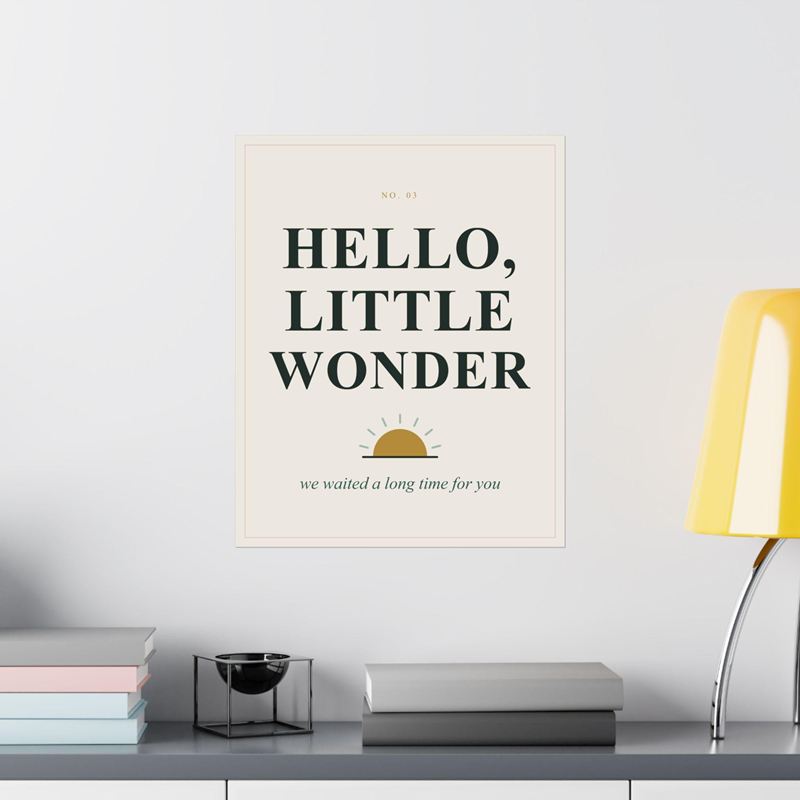 Cream nursery poster reading Hello, Little Wonder over a small gold sun, on a white wall beside a yellow lamp