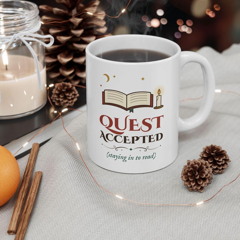 White mug printed with an open book, a candle and Quest Accepted (staying in to read), beside pine cones