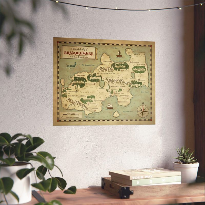 Parchment fantasy map print of a green island realm with forests, mountains and villages, on a wall above a desk