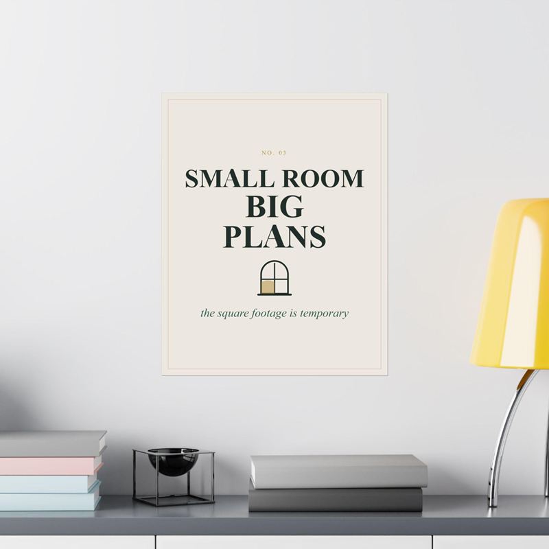 Cream poster reading Small Room Big Plans with a small arched window, on a white wall beside a yellow lamp