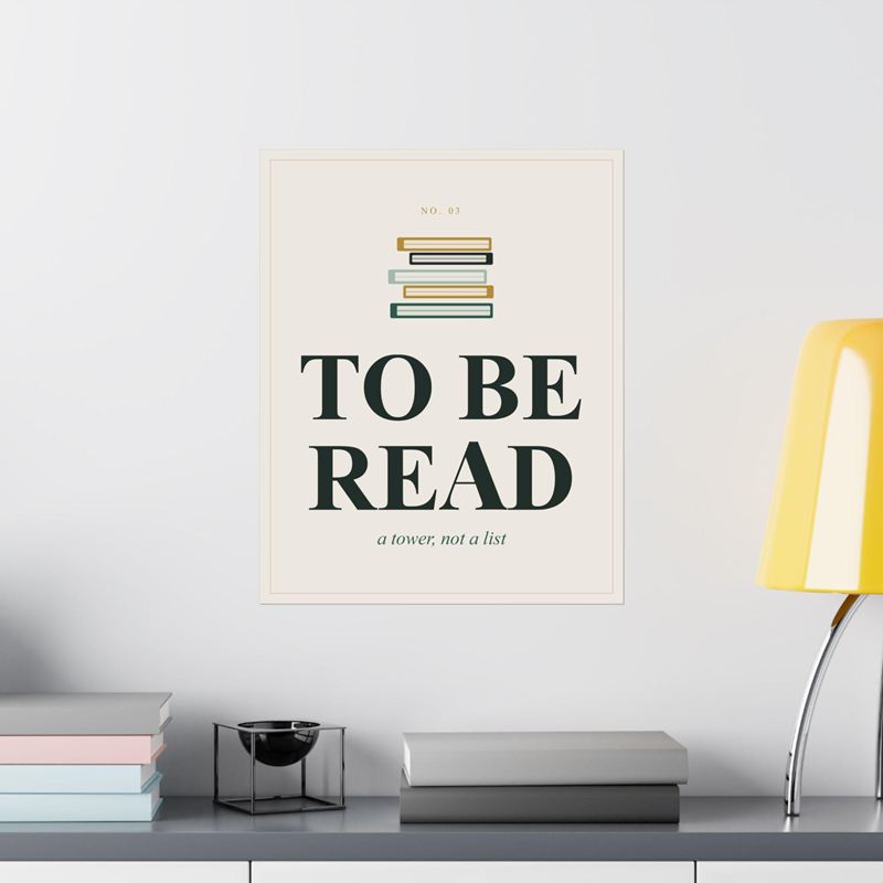 Cream poster with a stack of books above To Be Read and "a tower, not a list", on a white wall by a yellow lamp