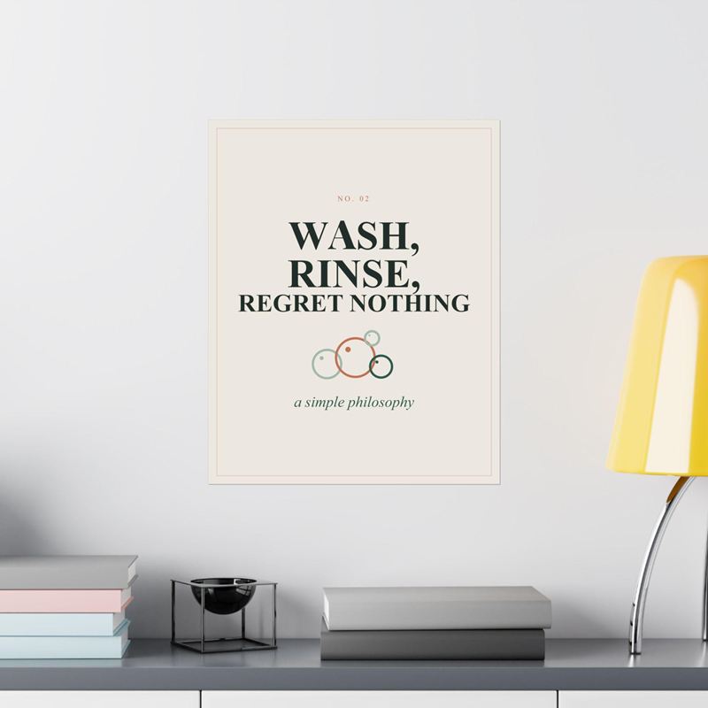 Cream poster reading Wash, Rinse, Regret Nothing with outlined soap bubbles, on a white wall beside a yellow lamp