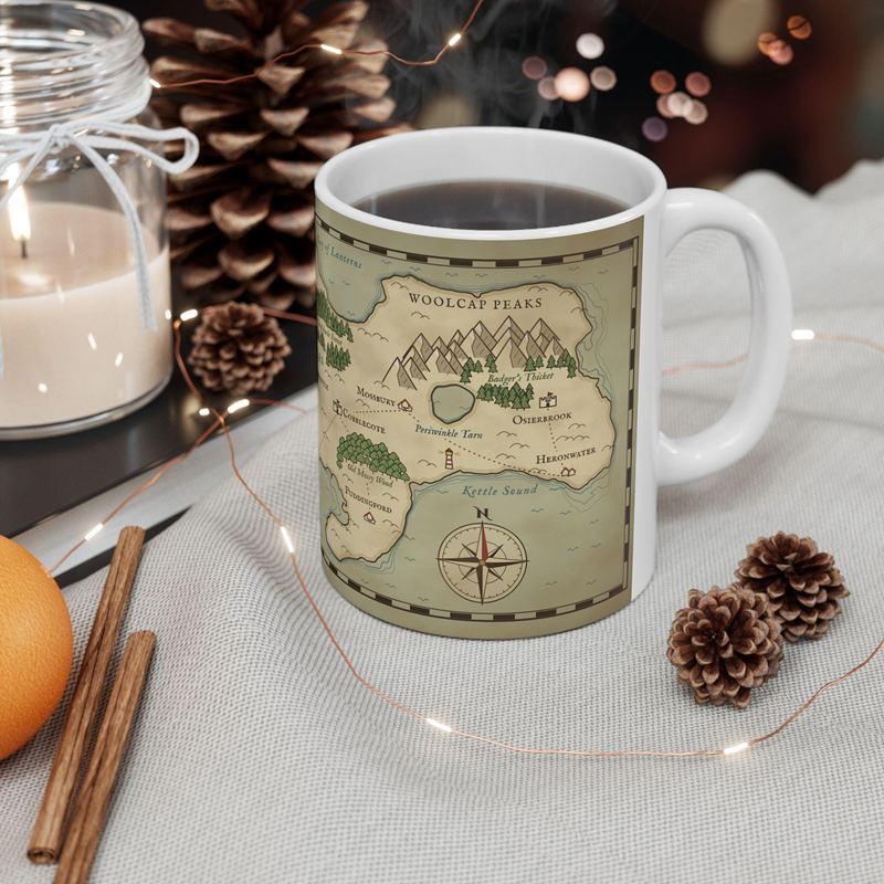 White mug wrapped in a parchment fantasy map with snowy peaks and a compass rose, full of coffee beside pine cones